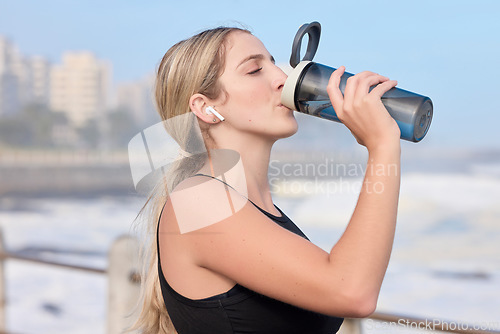 Image of Music, fitness and woman drinking water at the beach for sports, running and cardio routine. Podcast, bottle and thirsty female runner relax on workout break while streaming online motivation track