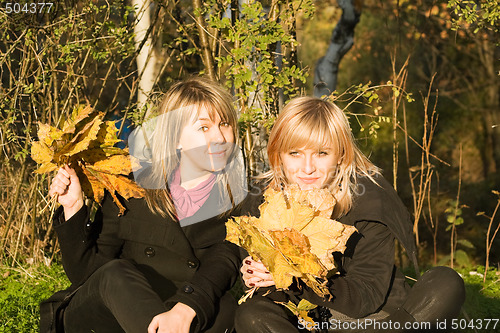 Image of Two young women with autumn leaves in park
