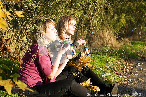 Image of Two young women starts up soap bubble in park