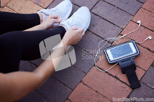 Image of Phone, fitness and footwear from above with a woman athlete sitting on the ground to tie laces. Exercise, music and getting ready for running with a female sports person outdoor for cardio training
