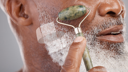 Image of Face roller, closeup and senior man with skincare, stone and dermatology product for skin glow. Elderly, cheek and facial roll of African male model doing self care for grooming with jade for beauty