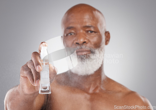 Image of Portrait, beauty and serum with a senior man holding an antiaging product in studio on a gray background. Face, skincare and cosmetics with a mature male spraying a facial treatment for beard care