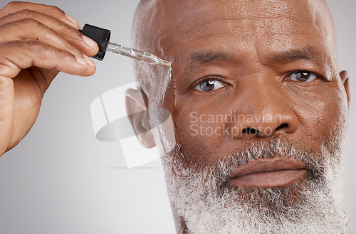 Image of Skincare, portrait and male with face oil in a studio for a natural, beauty and skin treatment. Cosmetic, health and senior man model with facial serum for a wellness routine by a gray background.