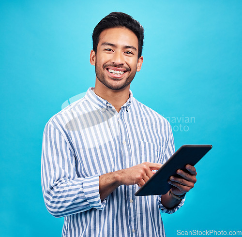 Image of Tablet, Asian man and smile portrait in a studio on social media, internet and website app scroll. Happiness, isolated and blue background with a male model reading technology for digital networking