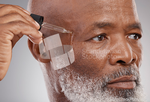 Image of Skincare, self care and man with face serum in a studio for a natural, beauty and skin treatment. Cosmetic, health and senior male model with facial oil for a wellness routine by a gray background.