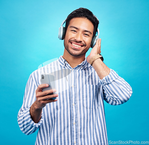 Image of Happy man in portrait, smartphone and headphones, listen to music with entertainment on blue background. Male person with smile, wireless technology and online audio streaming with radio or podcast