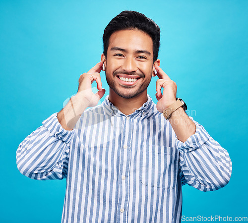 Image of Portrait, earphones and happy man with music in studio, relax and smile on blue background. Radio, face and asian male listening to podcast, streaming or audio, online or subscription while isolated