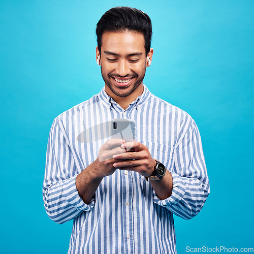 Image of Happy man, smartphone and earphones, music and social media with entertainment and chat on blue background. Male person with smile, wireless technology and online audio streaming with texting on app