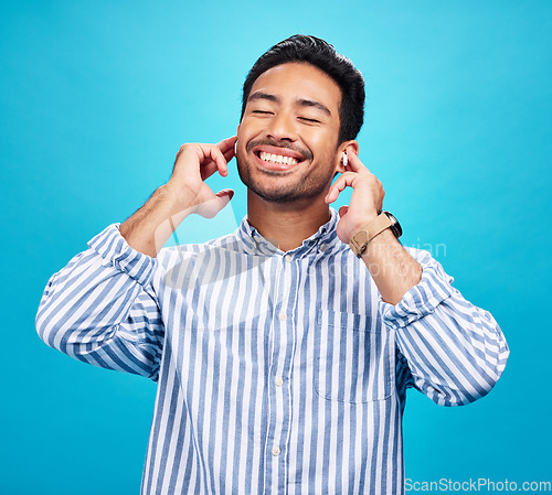 Image of Happy man, earphones and and music in studio, relax and cheerful on blue background. Radio, smile and indian male smile while listening to podcast, streaming or audio, online or subscription isolated