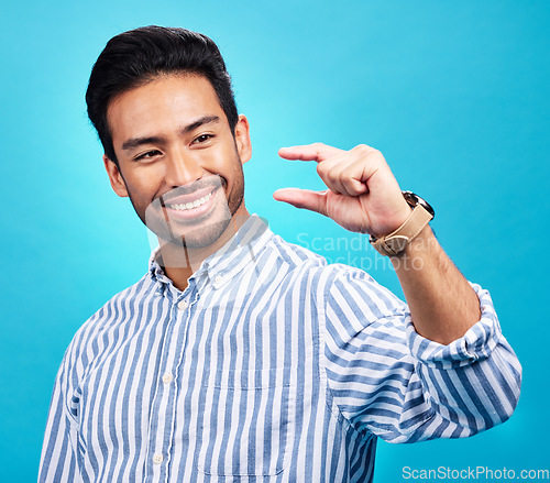 Image of Small, hand and gesture of a man with a smile in studio showing a tiny measurement. Isolated, blue background and male model show happiness and positive opinion with hands from small size sign