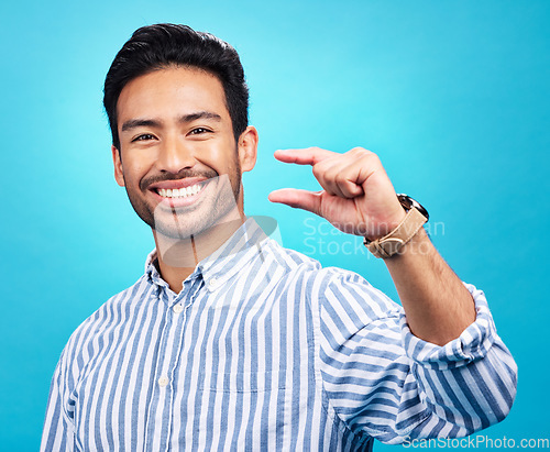 Image of Small, hand and gesture of a man portrait with a smile in studio showing a tiny measurement. Isolated, blue background and Asian model with happiness, positive opinion and hands show of pinch size