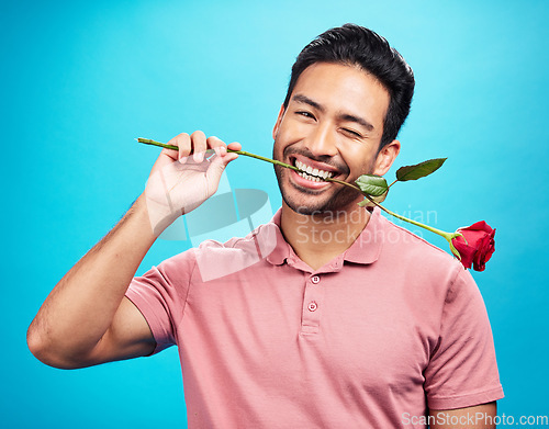 Image of Teeth, rose and wink with portrait of man in studio for celebration, gift and romance. Funny, goofy and present with male and flower on blue background for happiness, smile and valentines day mockup
