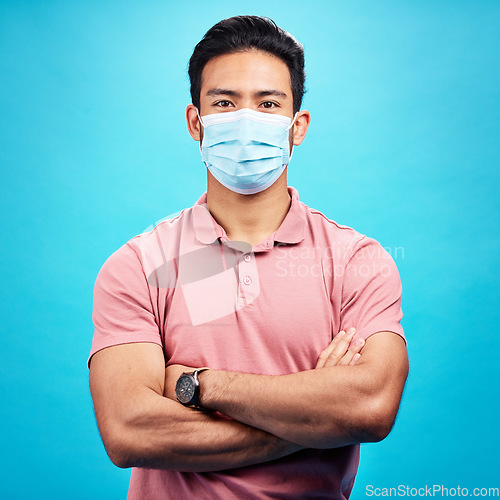 Image of Man in face mask, arms crossed in portrait and covid, safety from virus, bacteria and germs isolated on blue background. Disease, corona and male person, health compliance with protection in studio