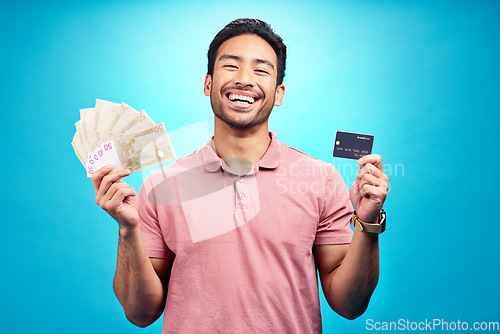 Image of Money, portrait and credit card by happy man in studio with savings, finance or investment growth on blue background. Cash, face and asian guy smile for banking, success or financial freedom isolated