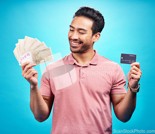 Image of Credit card, smile and money by happy man in studio with savings, finance or investment growth on blue background. Cash, profit and asian guy excited for banking, loan or financial freedom isolated