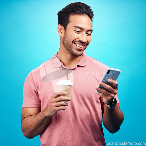 Image of Smile, coffee and man with phone in studio isolated on a blue background. Tea, cellphone and happiness of Asian person with drink, caffeine and mobile for social media, typing online or texting.