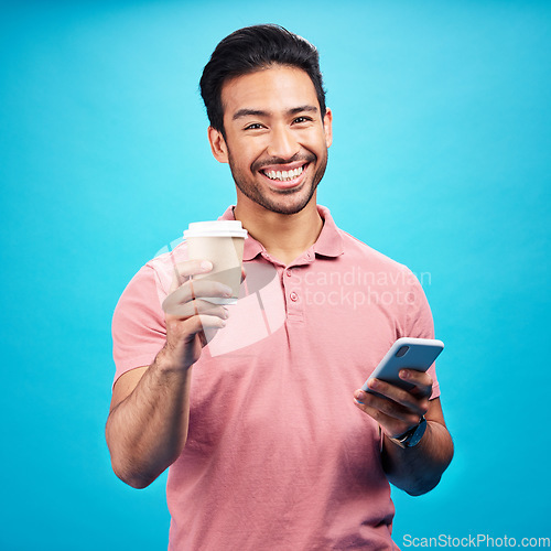 Image of Coffee, happiness and portrait of man with phone in studio isolated on a blue background. Tea, cellphone and smile of Asian person with drink, caffeine and mobile for social media or typing online.