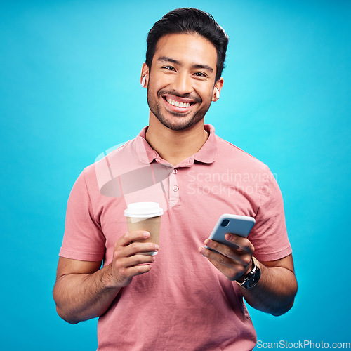 Image of Earphones, coffee and portrait of man with phone in studio isolated on a blue background. Tea, cellphone and happiness of Asian person with drink, caffeine and mobile for social media, music or radio