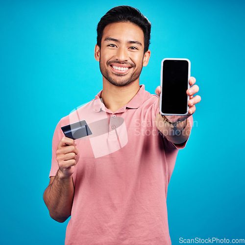 Image of Portrait, phone and credit card for online shopping with a man customer on a blue background in studio. Happy, smile and ecommerce with a young shopper using fintech to make a payment or transaction