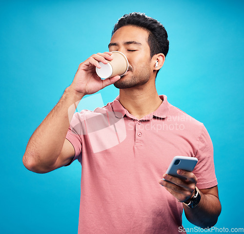 Image of Earphones, drinking coffee and man with phone in studio isolated on a blue background. Tea, cellphone and Asian person drink, caffeine or espresso with mobile for social media, radio music or podcast