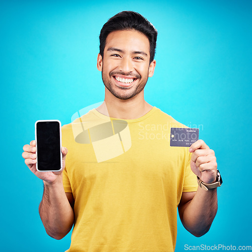 Image of Portrait, phone and credit card for ecommerce with a man customer on a blue background in studio. Happy, smile and online shopping with a young shopper using fintech to make a payment or transaction