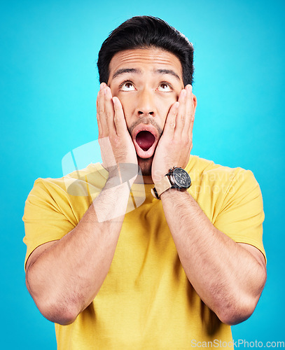 Image of Man, wow and shocked at surprise or announcement in studio with hands on face and mouth open. Male model person on a blue background while thinking of gossip, sale or promotion with comic emoji
