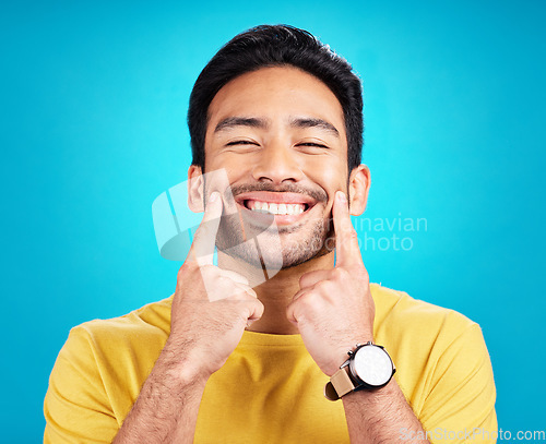 Image of Teeth, smile and pointing with a man on a blue background in studio for dental care or oral hygiene. Portrait, face and happy with a handsome young male at the dentist for tooth care or whitening