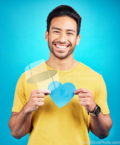 Image of Portrait, cutout heart and Asian man with support, wellness and confident person against blue studio background. Face, male model or guy with symbol for love, cheerful and emoji with smile and loving