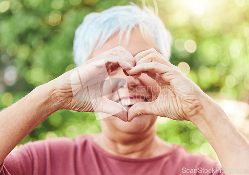 Image of Portrait, hands and heart with a senior woman outdoor in a garden during summer for love or health. Face, emoji and shape with a hand gesture by a happy mature female outside in a park for wellness