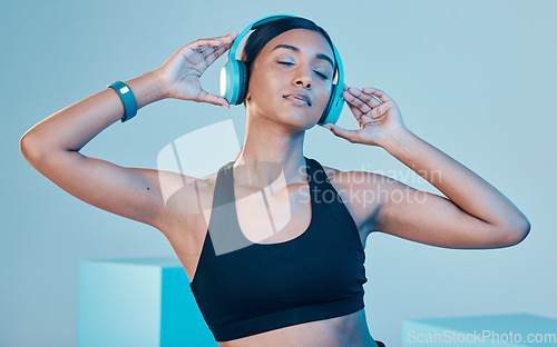 Image of Headphones, fitness and woman isolated on blue background for workout, training or exercise music. Gen z, sports and biracial person listening on audio technology, mental health or wellness in studio