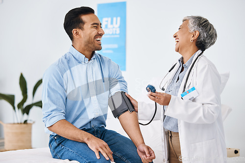 Image of Doctor, patient and blood pressure consultation in hospital while laughing and talking about health. Medical professional woman and man with cuff for hypertension, healthcare and wellness check