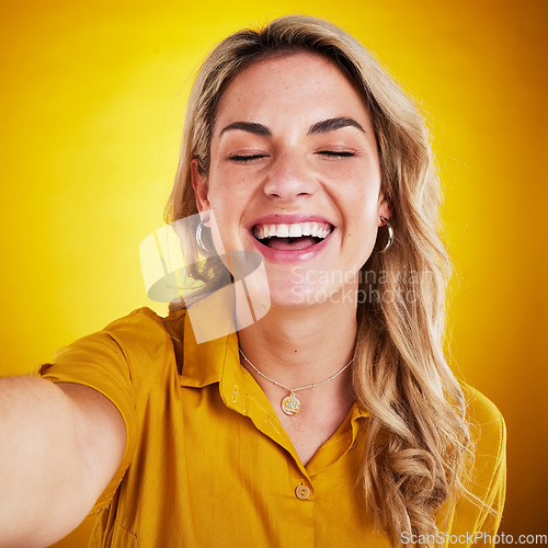 Image of Selfie, face and smile with a laughing woman on a yellow background in studio for fun or humor. Eye closed, comic and funny with an attractive young female model enjoying comedy, being silly or goofy