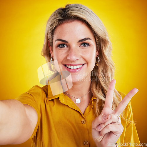 Image of Selfie, portrait and peace with a woman on a yellow background in studio looking happy. Face, smile and hand gesture with an attractive young female model showing v emoji, symbol or social media pov