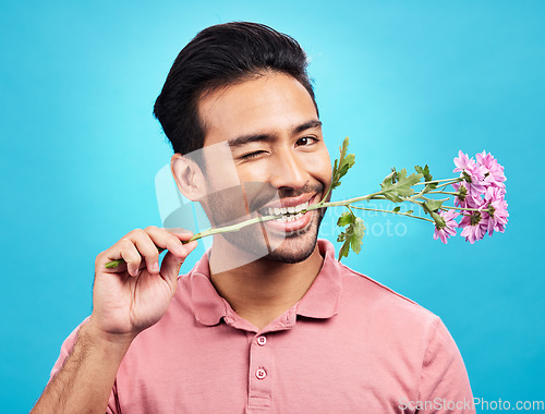 Image of Teeth, flower and wink with portrait of man in studio for celebration, gift and romance. Funny, goofy and present with male isolated on blue background for flirting, smile and valentines day mockup