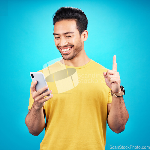 Image of Number one, phone and man isolated on blue background for online question, idea or decision on mobile app. Happy asian person or user with smartphone, internet or website and pointing up in studio