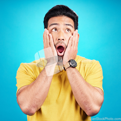 Image of Wow, shocked and man with hands on face and mouth open for surprise or announcement in studio. Male model person on a blue background while thinking of gossip, sale or promotion with comic emoji