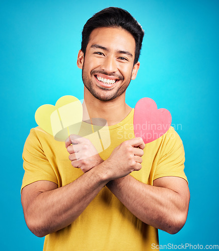 Image of Portrait, smile and man with heart cutout in studio isolated on a blue background. Love, happiness and Asian person with symbol, sign or emoji for affection, care and romance, empathy and valentines.