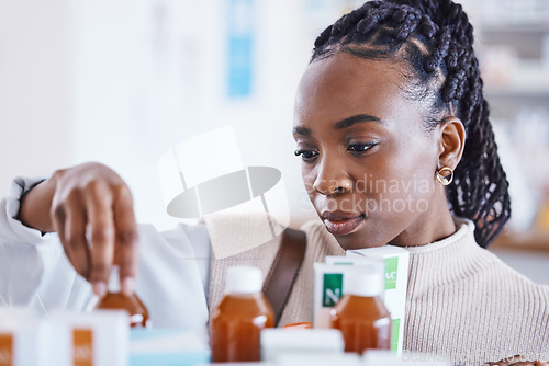 Image of Serious black woman, patient and medication on shelf for cure, illness or pain relief at pharmacy. African American female reading or looking at pharmaceutical products, medicine or drugs at clinic