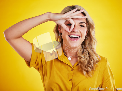 Image of Portrait, happy woman and okay on eyes for good review, motivation and sign on yellow background. Female person, funny face and ok hands for agreement, support and yes to emoji, thank you or winning