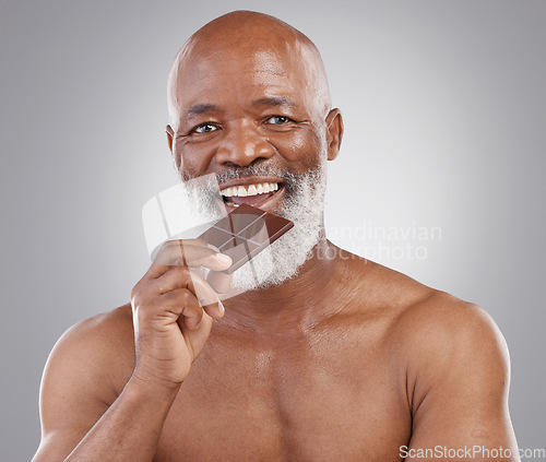 Image of Black man, senior portrait and eating chocolate isolated on a studio background for a treat. Happy, snack smile and an elderly African model biting into a sweet candy bar for happiness and sugar