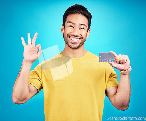 Image of Credit card, okay and portrait of man isolated on blue background for shopping, e commerce and payment loan. Happy asian person, excited for banking solution, financial savings and ok emoji in studio