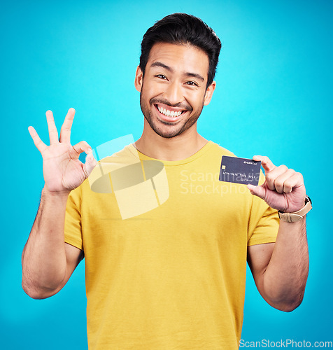 Image of Ok, credit card and man in portrait isolated on blue background for shopping, e commerce and payment loan. Happy asian person, excited for banking solution, financial savings and okay emoji in studio