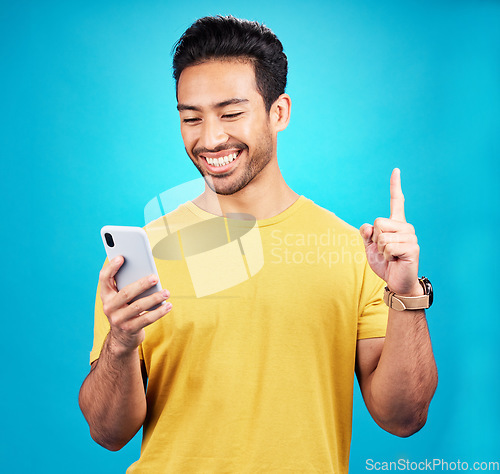 Image of Asian man, phone and man pointing up with idea, solution or question against a blue studio background. Happy person or user on mobile smartphone, internet or website and point for solving on mockup
