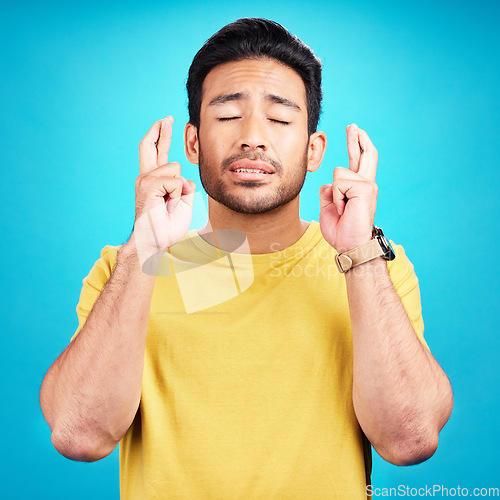 Image of Hope, man and fingers crossed for luck in studio isolated on a blue background. Wish, hand gesture and male person with aspiration, hoping emoji and wait for good fortune, result or optimistic faith.