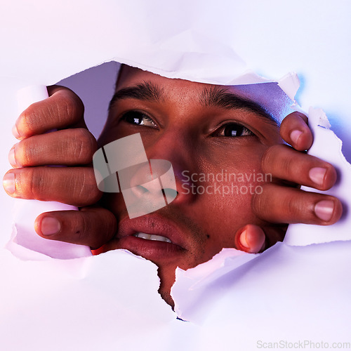 Image of Face, wall and a man looking through a hole to discover, explore or search while on an adventure. Head, eyes and thinking with a handsome young male closeup in studio to look out from a tear or gap