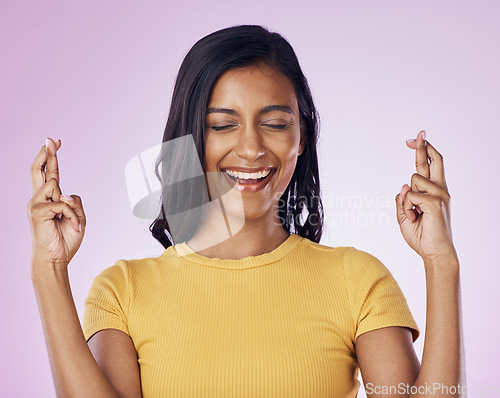 Image of Fingers crossed, wish and woman in a studio with hope, prayer or faith for success or achievement. Happy, smile and Indian female model with a luck hand gesture or sign isolated by purple background.