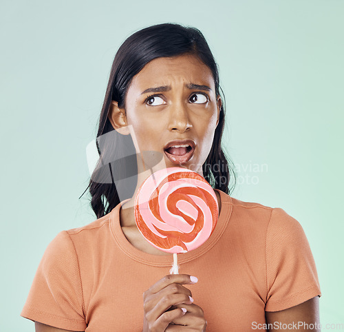 Image of Thinking, lollipop and woman with candy in studio isolated on a green background. Idea, sweets and Indian person with snack, delicious sucker or sugar treats, dessert or confectionery junk food.