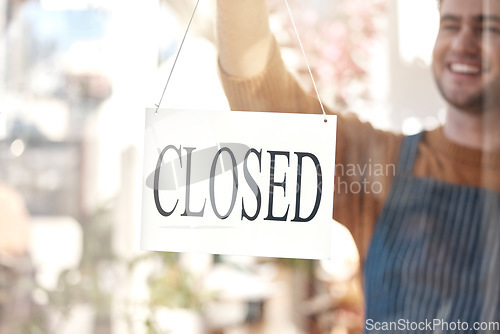 Image of Closed, sign and happy man at shop, store and notice of retail closing time, board and advertisement. Closeup of employee advertising end of business to public, signage or information on glass window