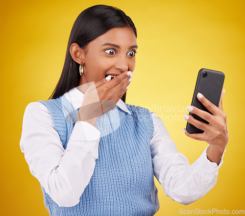 Image of Wow, surprise and woman with phone in studio space reading text or email on yellow background. Technology, communication and good news, happy Indian girl with social media gossip or online content.