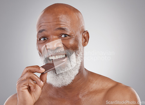 Image of Black man, portrait and eating chocolate sweets isolated on a studio background for a treat. Happy, snack smile and an elderly African model biting into a sweet candy bar for happiness and sugar